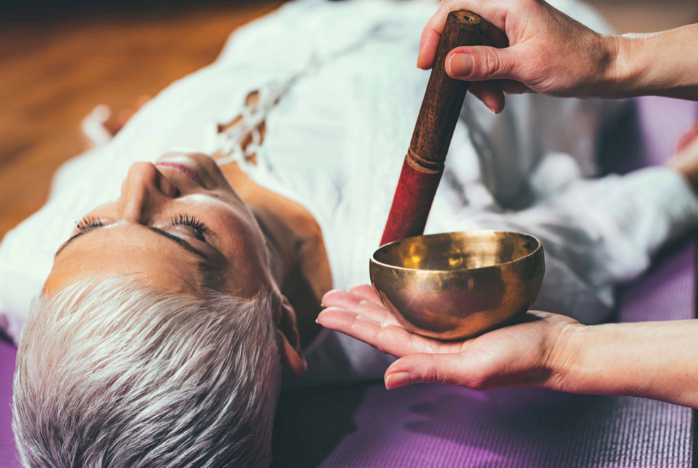 Photo of a woman having a sound bath with someone holding a small Tibetan sound bowl near their head