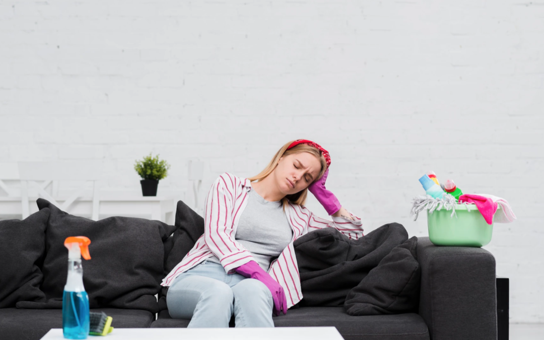 A woman on the sofa looking miserable with cleaning equipment all around her